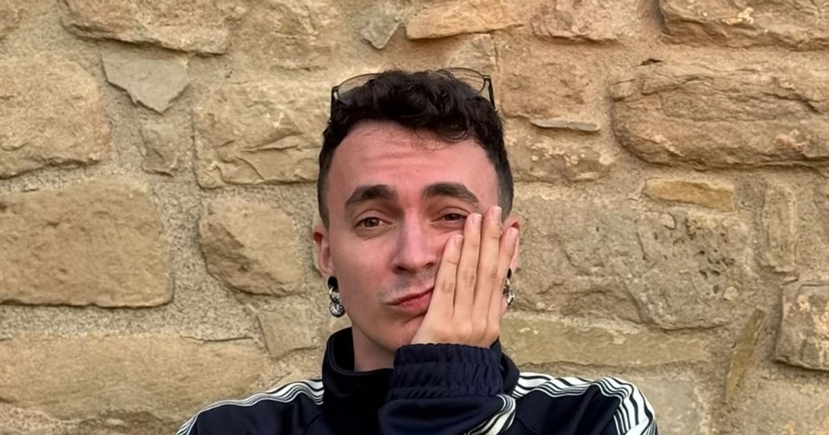 Arnau Palacín amb la mà a la galta i una jaqueta esportiva fosca, davant d’un mur de pedra