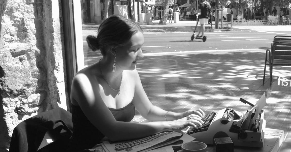 Mireia Riu escrivint amb una màquina d’escriure dins d’una cafeteria, al costat de l’aparador